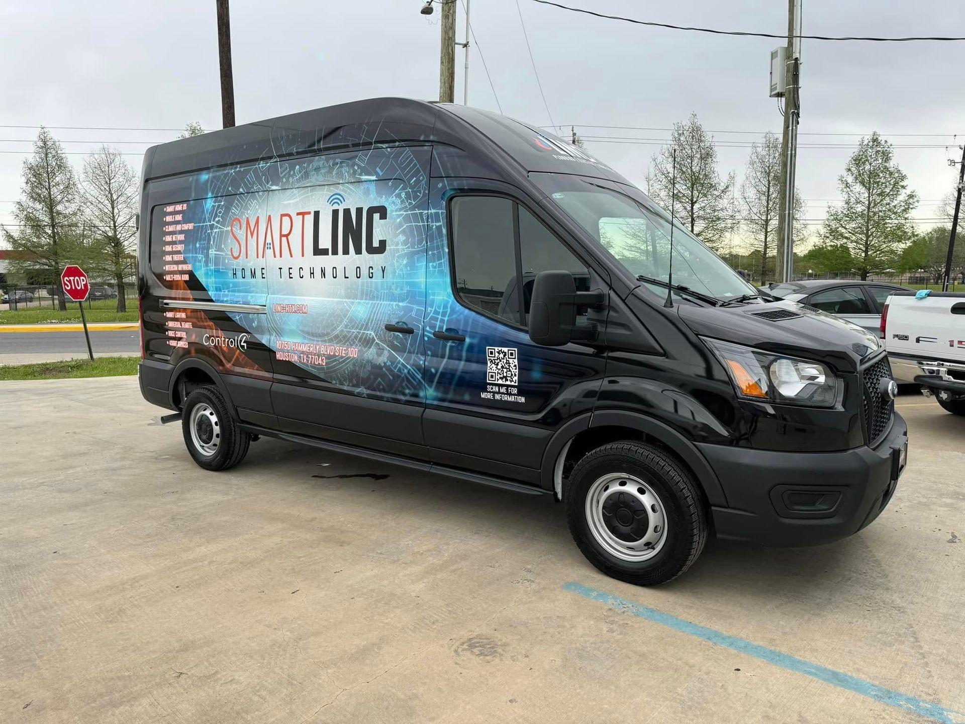 A black cargo van parked in a lot, featuring a large blue and white "SMARTLINC" branding wrap on its side.