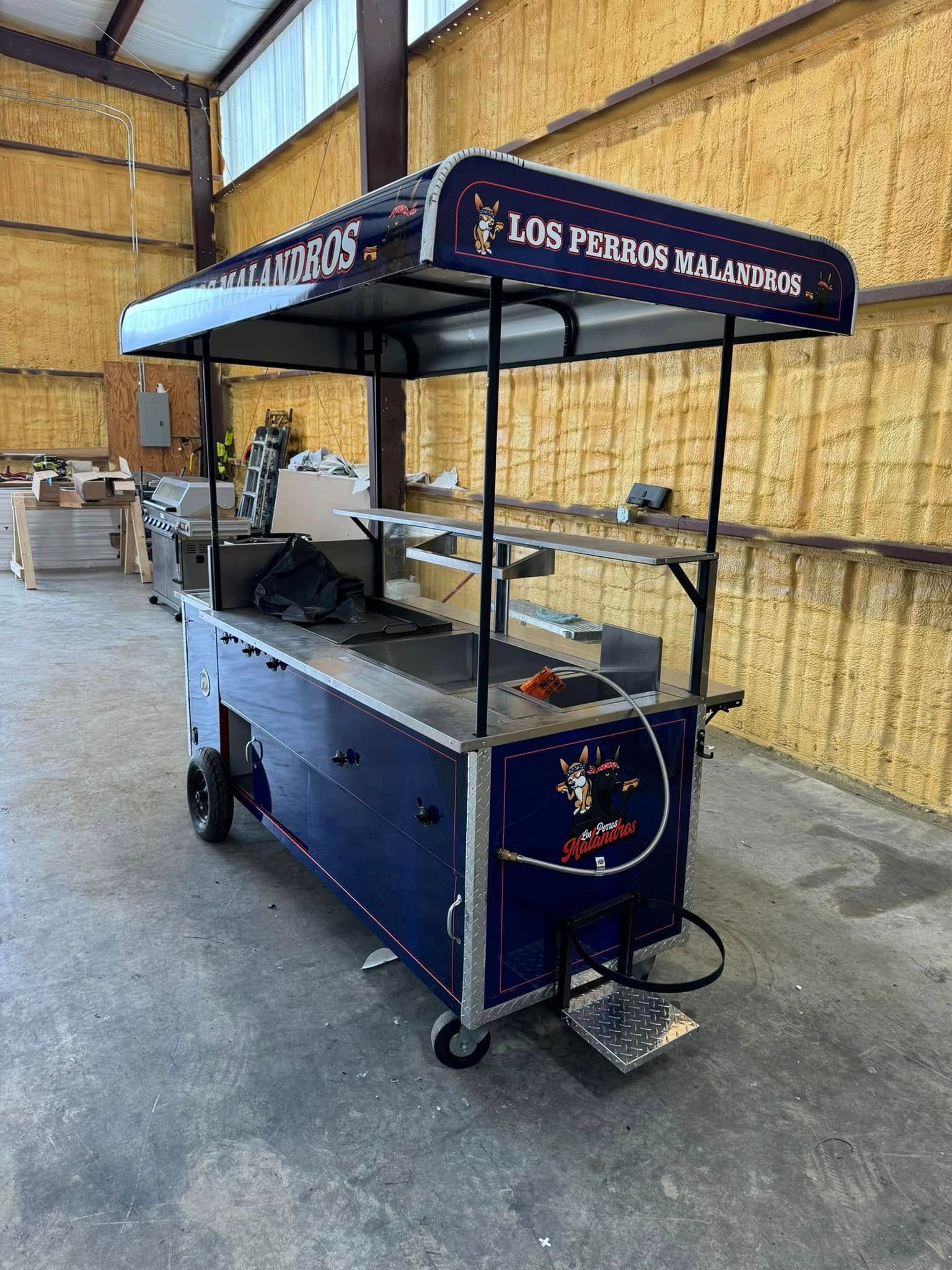 A dark blue mobile street food cart with a roof, standing in an industrial warehouse setting.