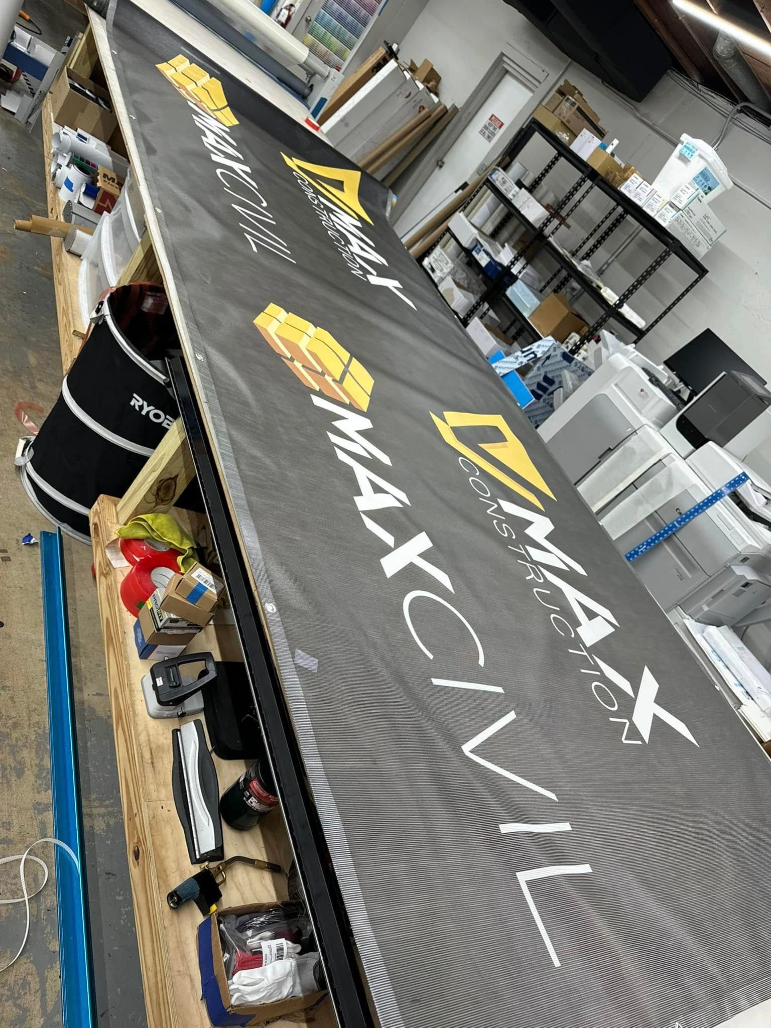 A silver, 3D metallic logo featuring two stylized human figures within a circle on a dark gray wall.