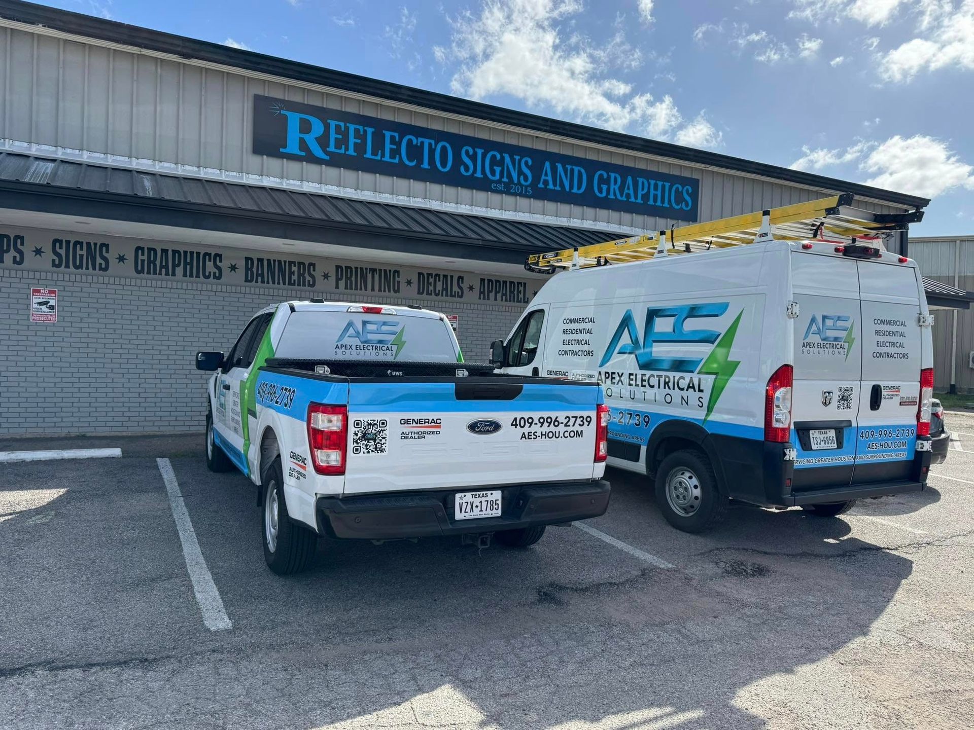Two white service vehicles with blue and green branding parked in front of a Reflecto Signs and Graphics storefront.