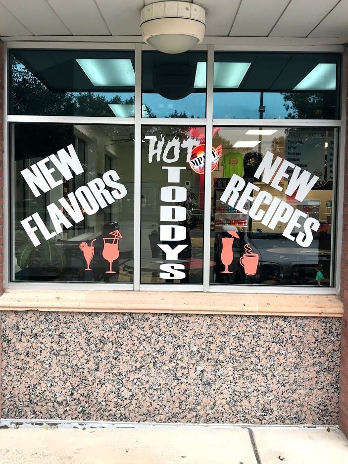 A person in a blue uniform applies protective film to a grey car fender using a squeegee in a professional garage.