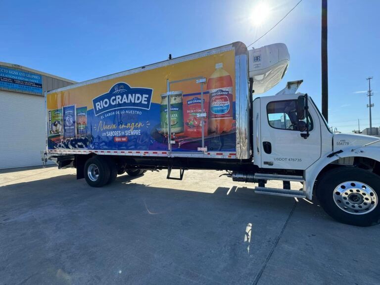 A white box truck parked on a concrete lot, featuring a large yellow and blue advertisement for Rio Grande food products.