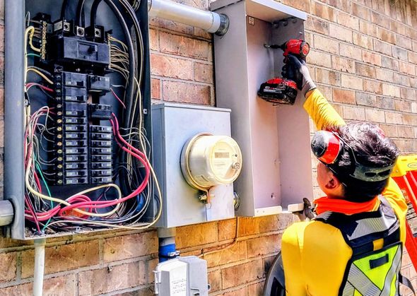 A photo of an electrician holding a milwaukee impact drill installing a service