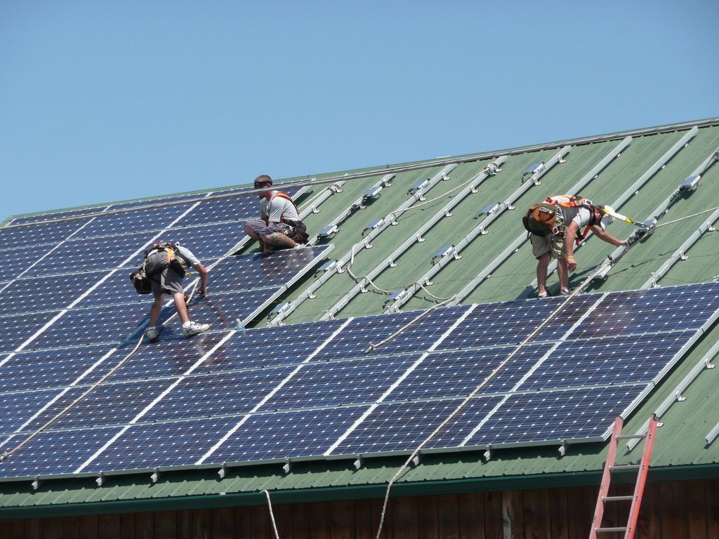 Three men are installing solar panels on the roof of a building