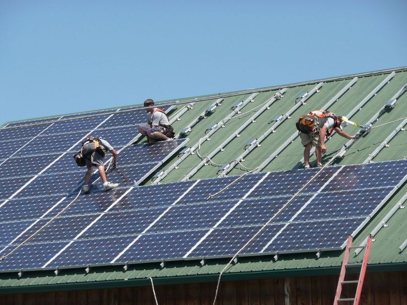 A photo of electricians installing solar panels on a roof