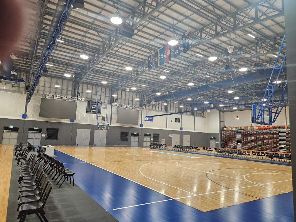 A Large Indoor Basketball Court With a Wooden Floor and Blue Lines — Nick Favot Painting in Bohle, QLD