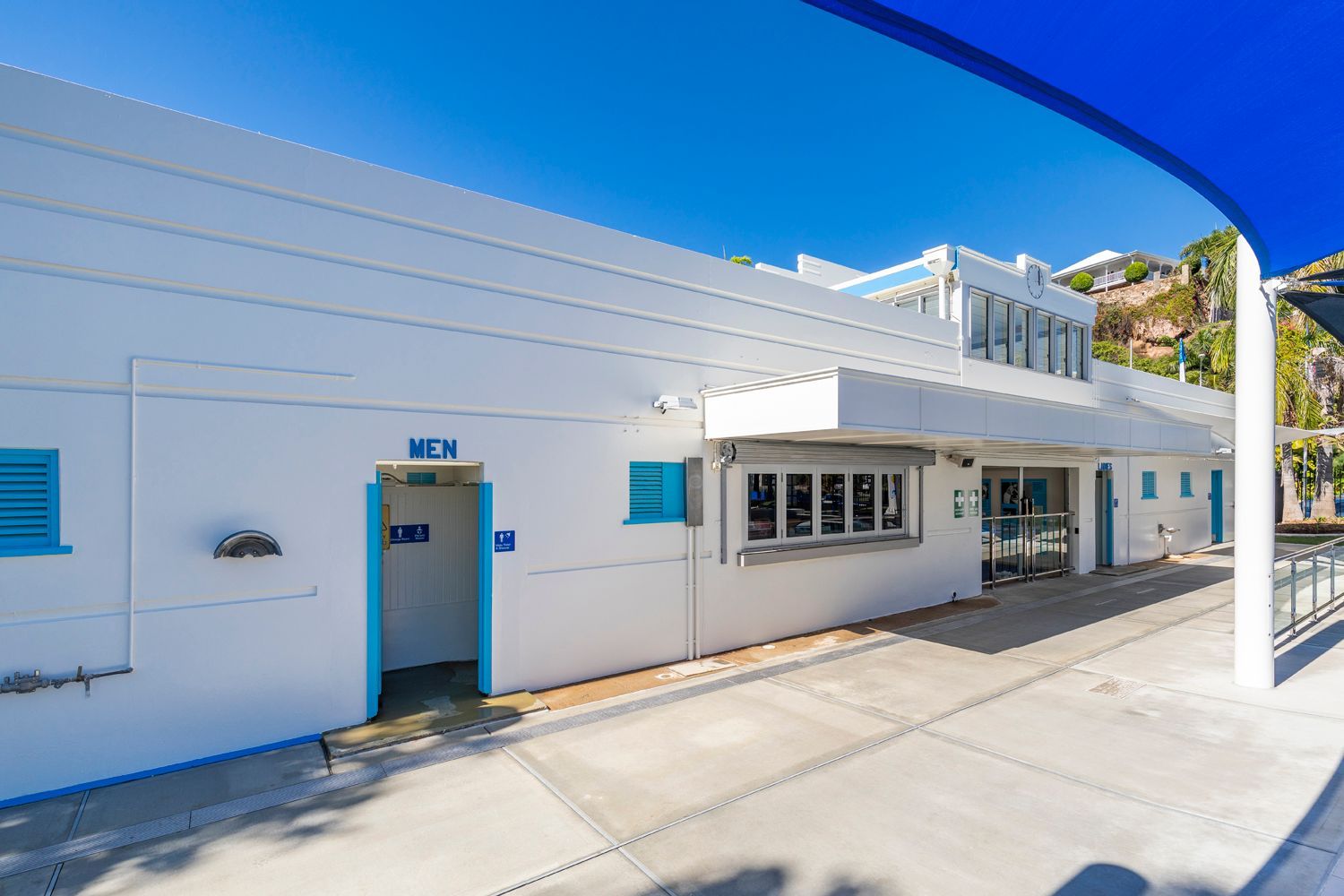 White building with blue accents; public restroom, windows, and a partially visible blue canopy. Bright sunny day — Nick Favot Painting in Bohle, QLD