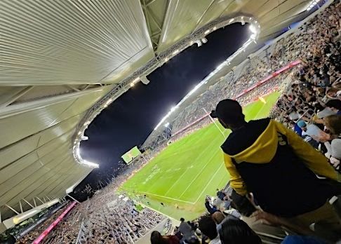 A Man in a Yellow Jacket is Watching a Soccer Game in a Stadium — Nick Favot Painting In Bohle, QLD