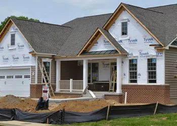 House under construction; exterior with Tyvek wrap, brick accents, and a porch.