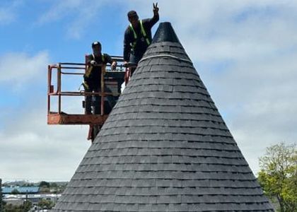 Two men are standing on top of a large cone roof.