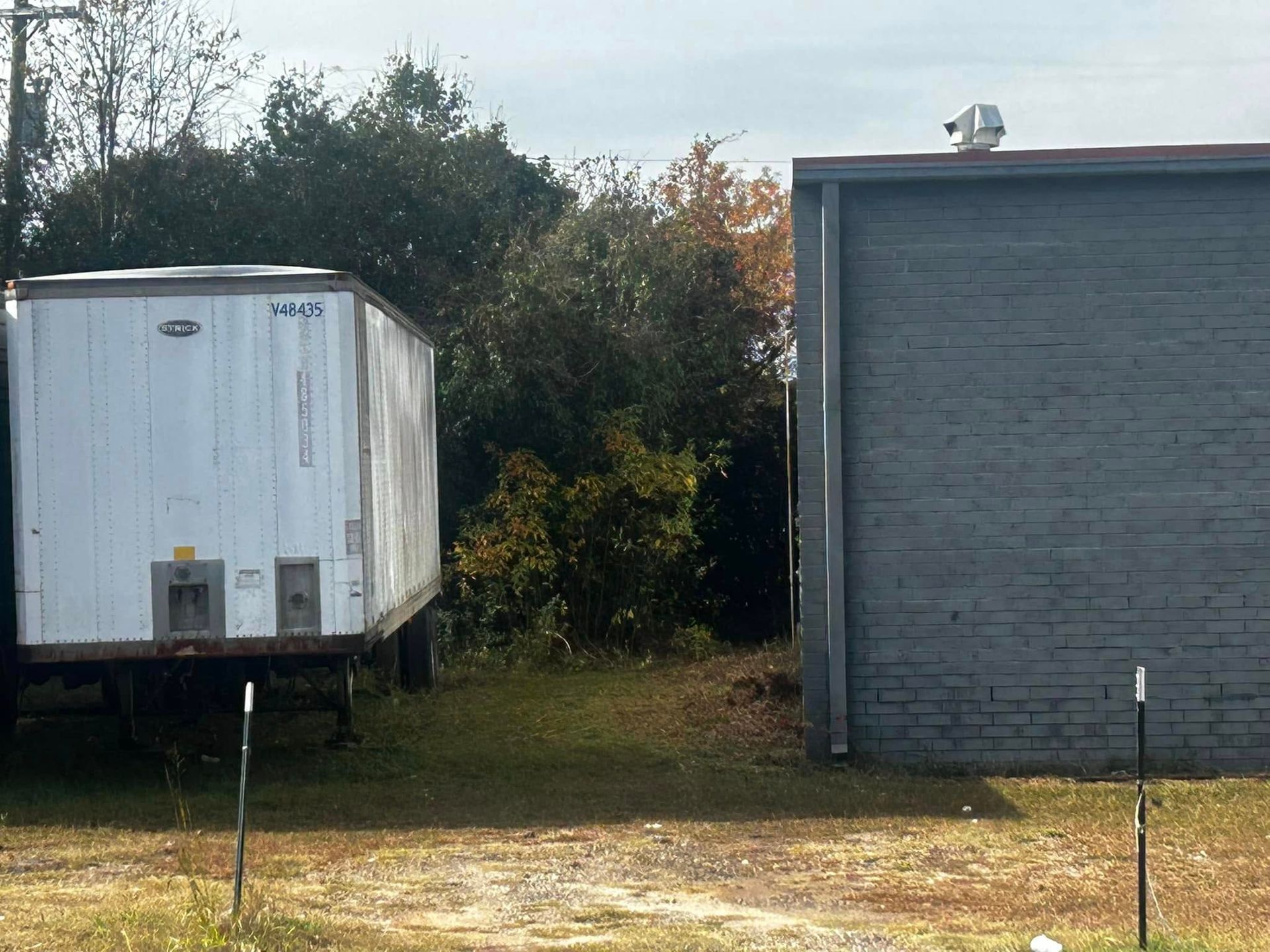 White trailer and gray building next to trees, under a blue sky.