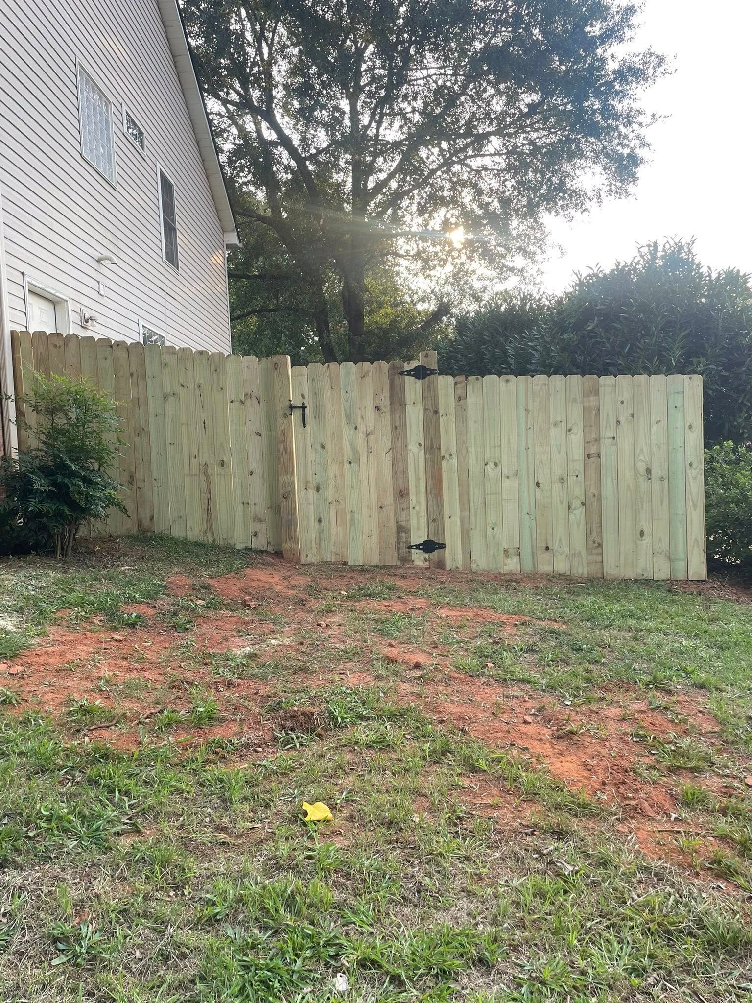 Wooden fence with gate in front of a house. Sunlight shines through trees in the background.