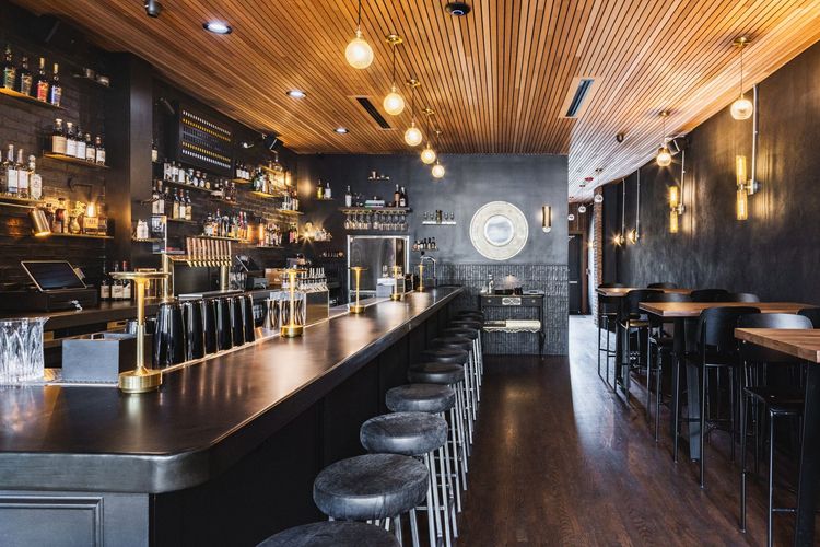 The interior of a restaurant with a long bar and stools.