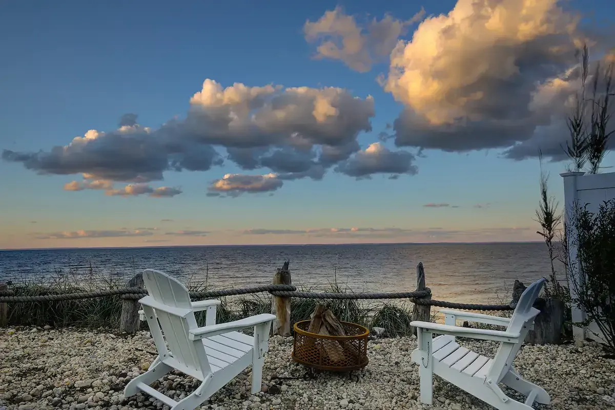 Two white chairs are sitting on a rocky beach overlooking the ocean.