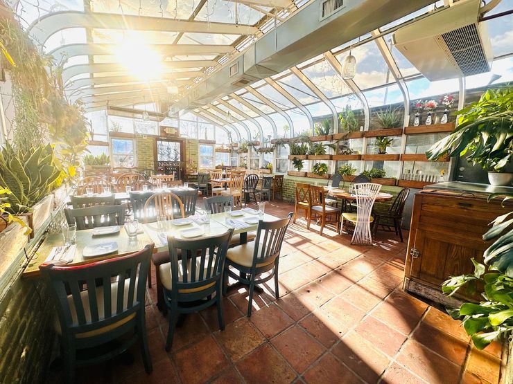 A restaurant with tables and chairs inside of a greenhouse.