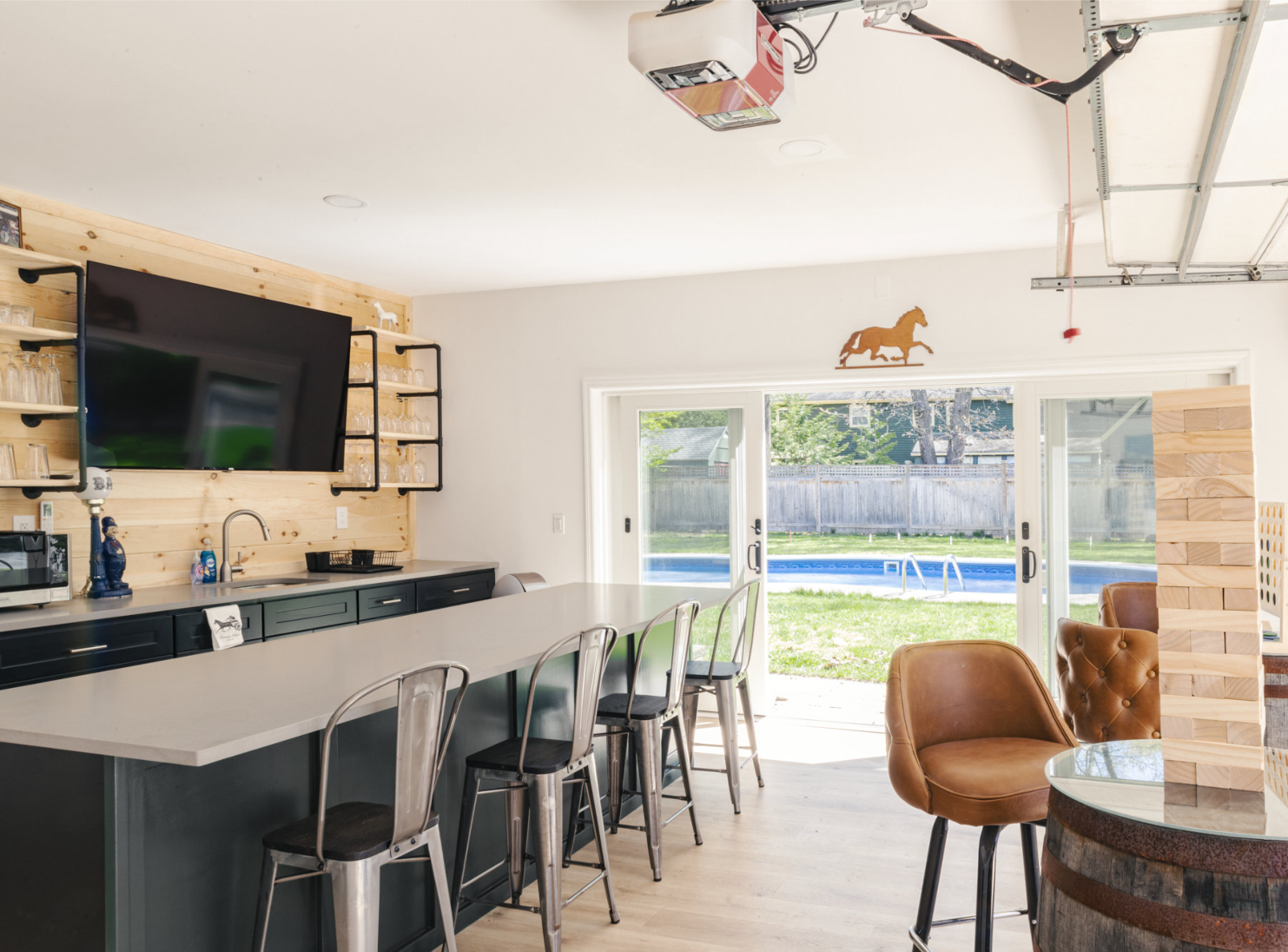 A kitchen with a bar , chairs , a television and a sliding glass door leading to a pool.