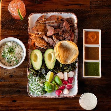 A plate of food on a wooden table with a drink in the background