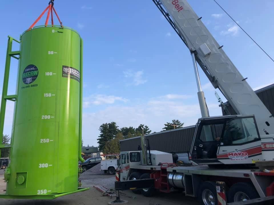 A crane truck lifts a lime green RECON gas cannister 
