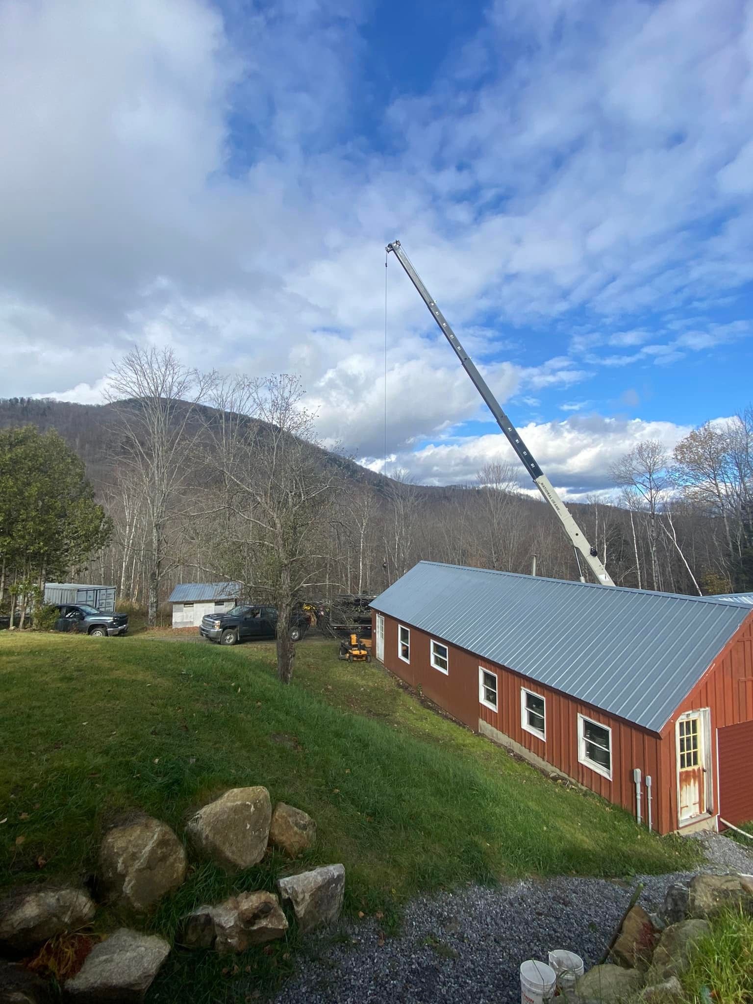 A large crane in use sits behind a red barn  in Vermont