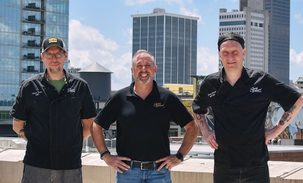 Three men are standing in front of a building.