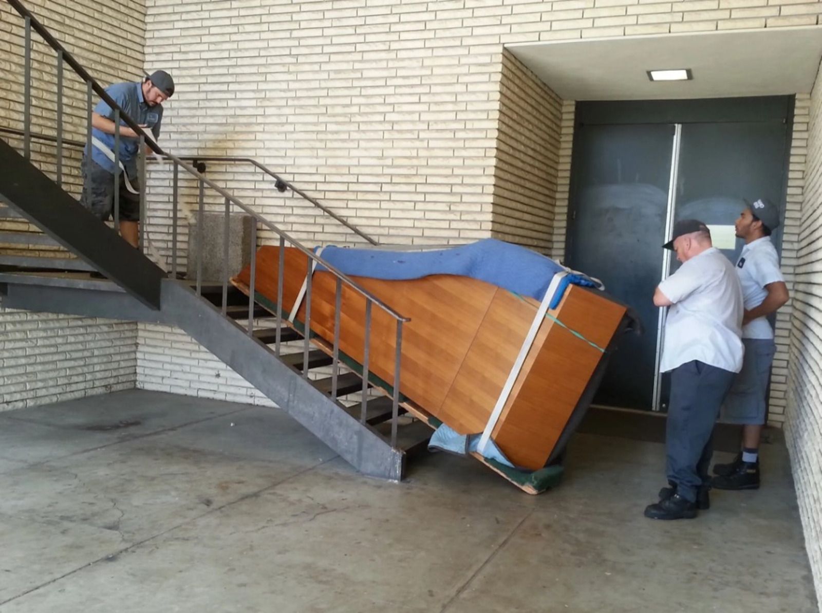 Three people move a wooden dresser down a staircase. One person guides from above, two below.