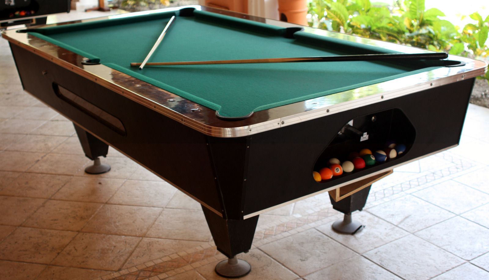 Black pool table with green felt, balls in rack, cue resting on the surface.