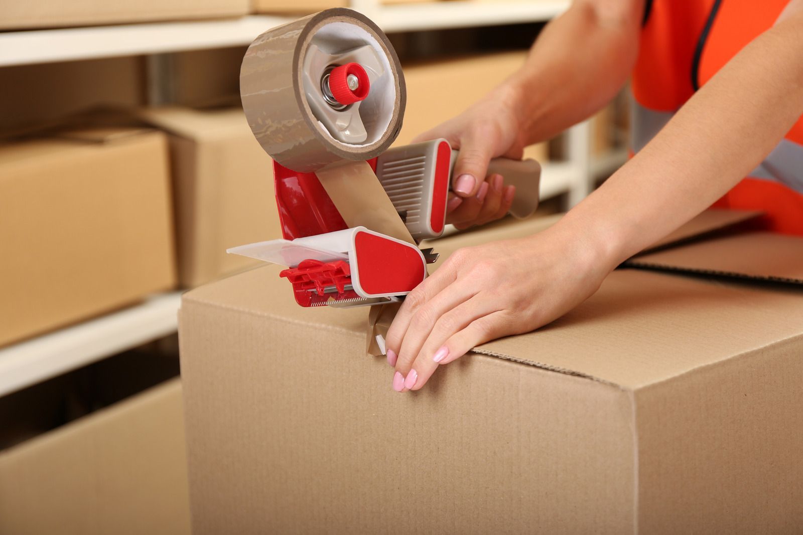 Person taping a cardboard box with a tape dispenser in a warehouse setting.