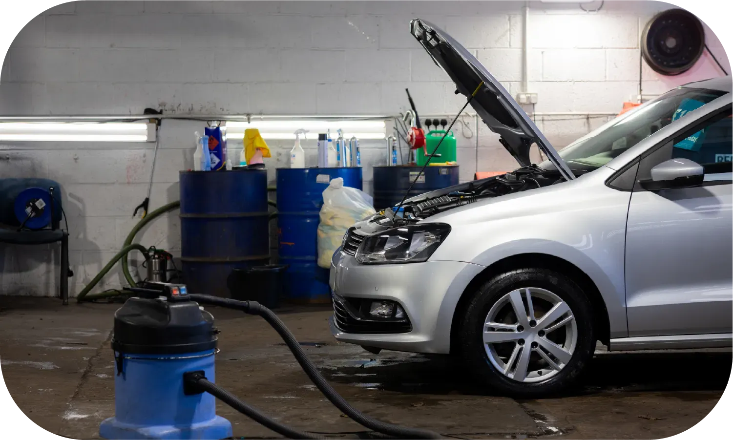 A car is being cleaned in a garage with the hood open.