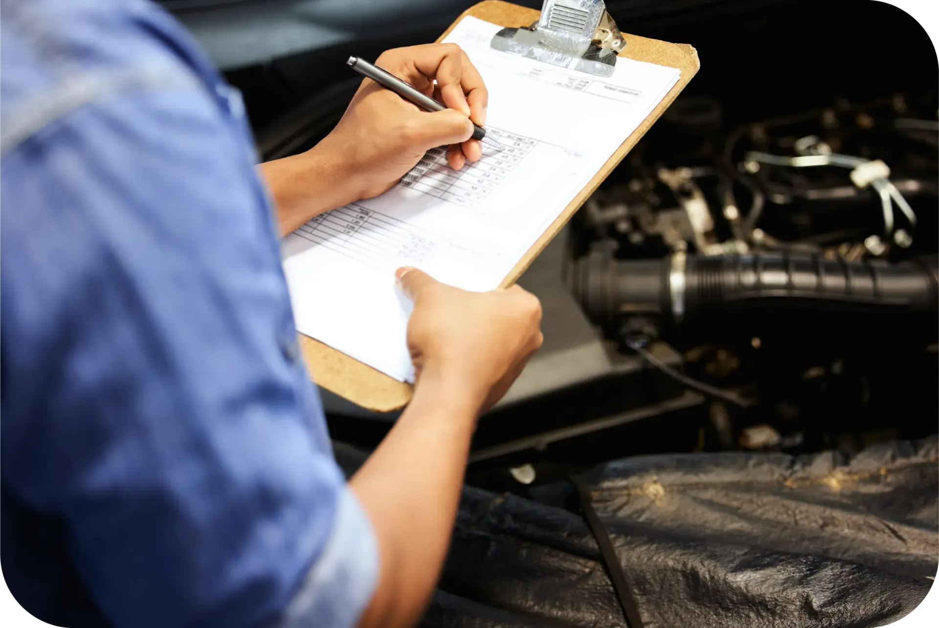 A man is writing on a clipboard in front of a car engine.