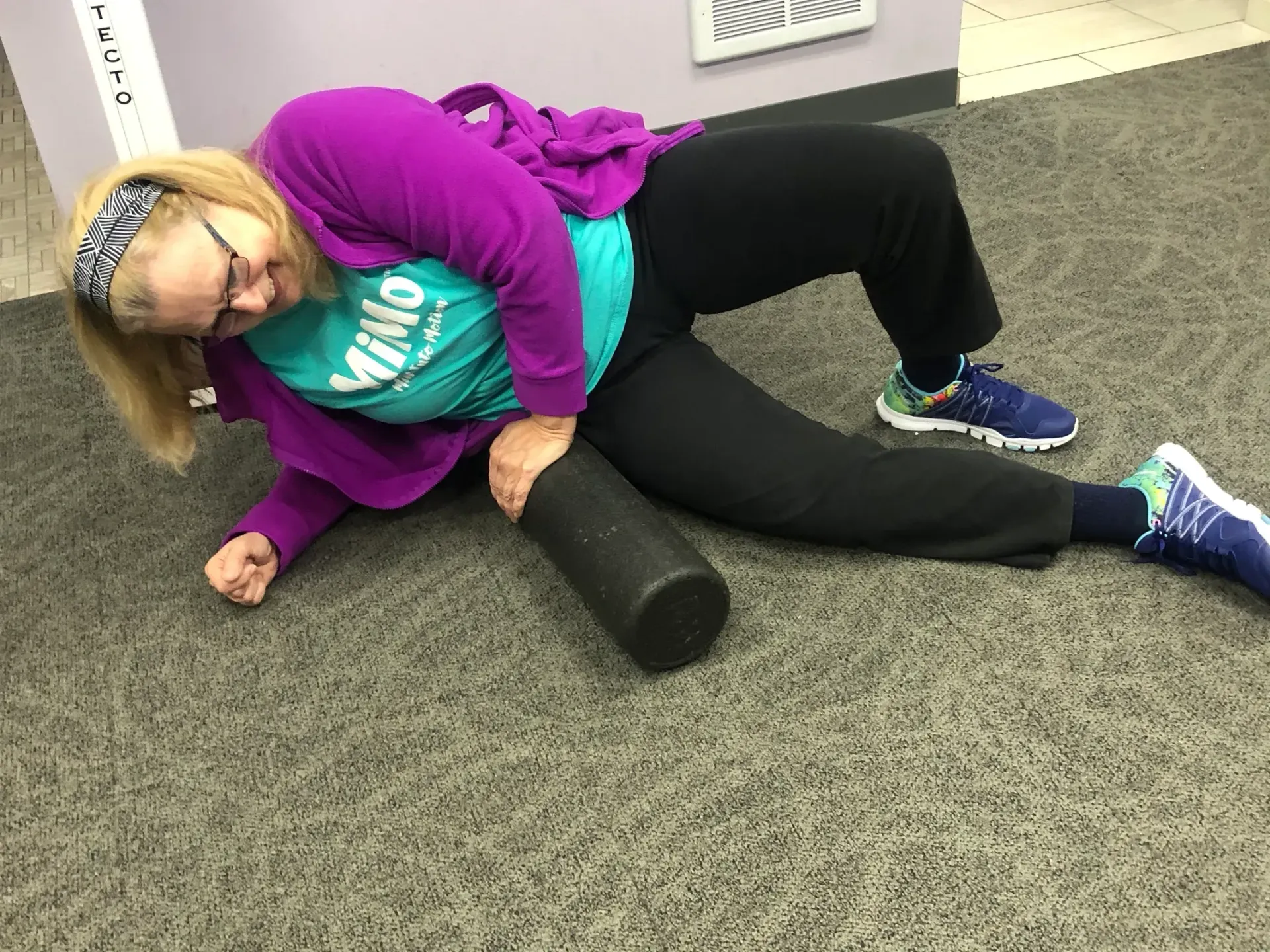 A woman is laying on the floor using a foam roller.