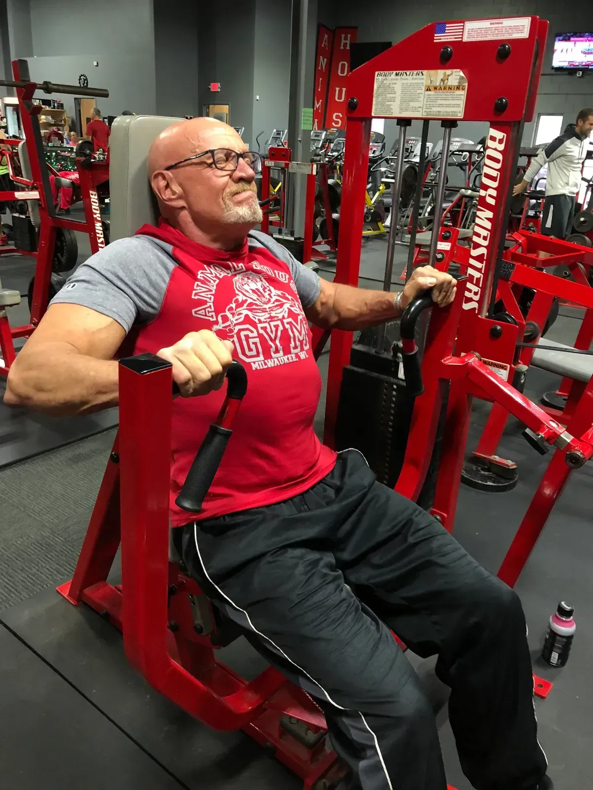 A man in a red gym shirt is using a machine