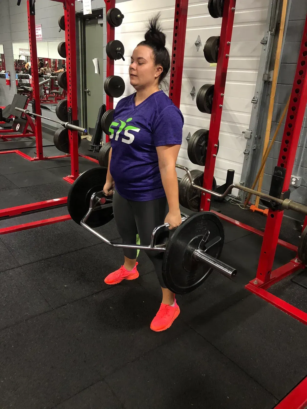 A woman in a purple shirt is lifting a barbell in a gym.