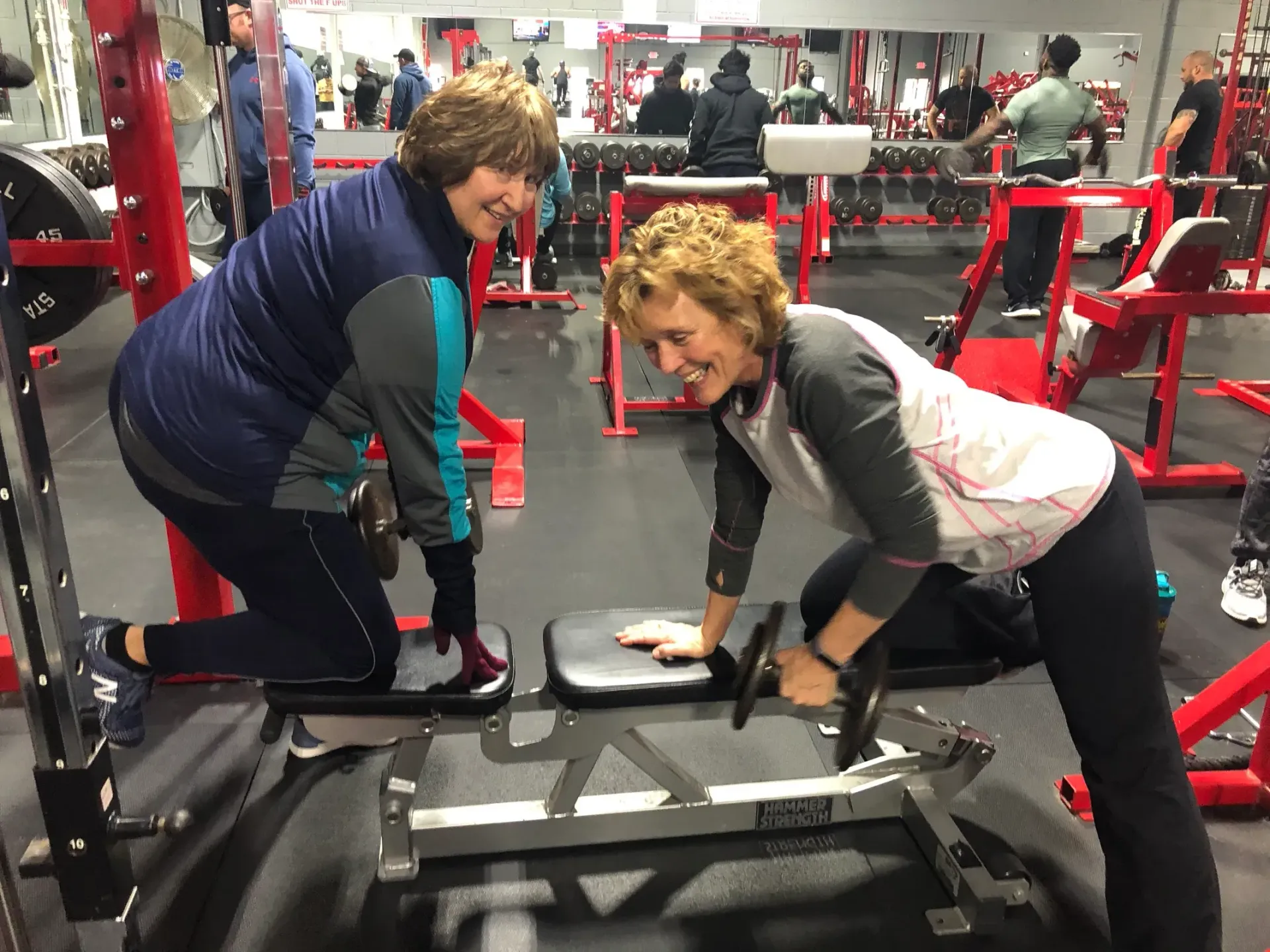 Two women are doing exercises on a bench in a gym.