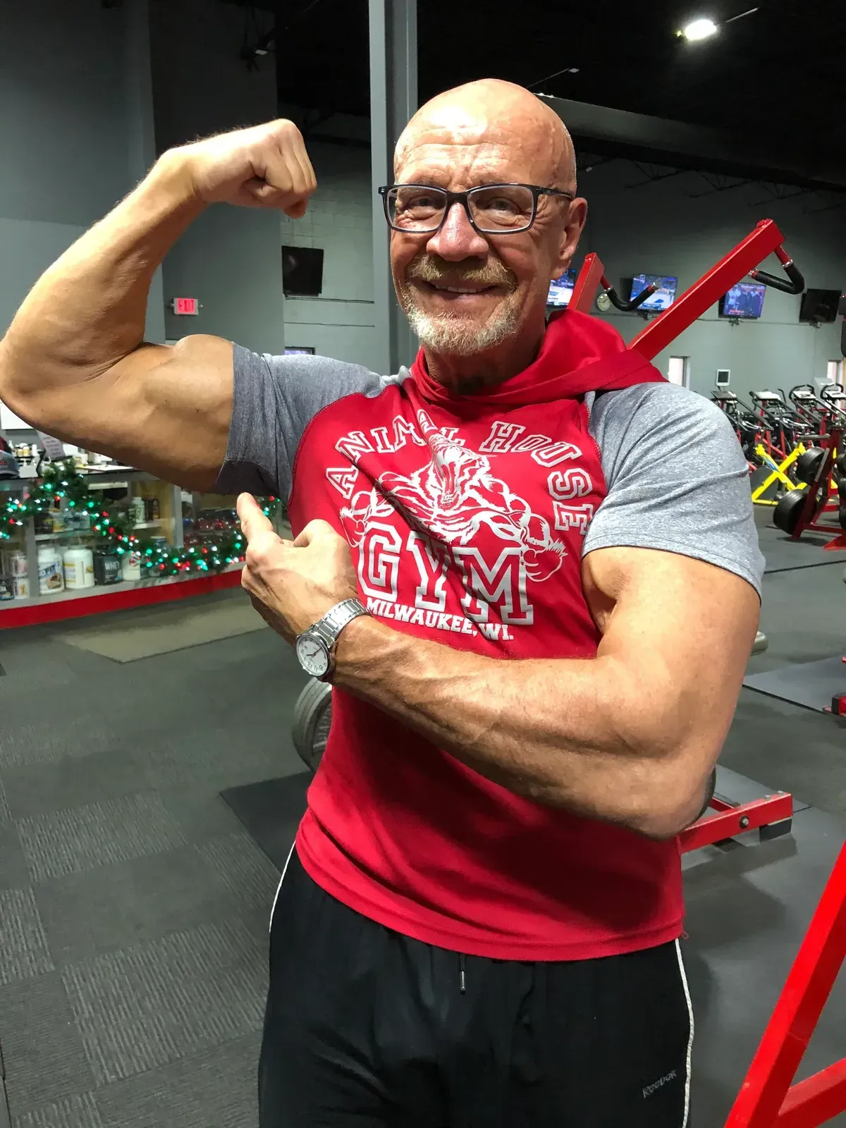 A man wearing a gym shirt is flexing his muscles in a gym