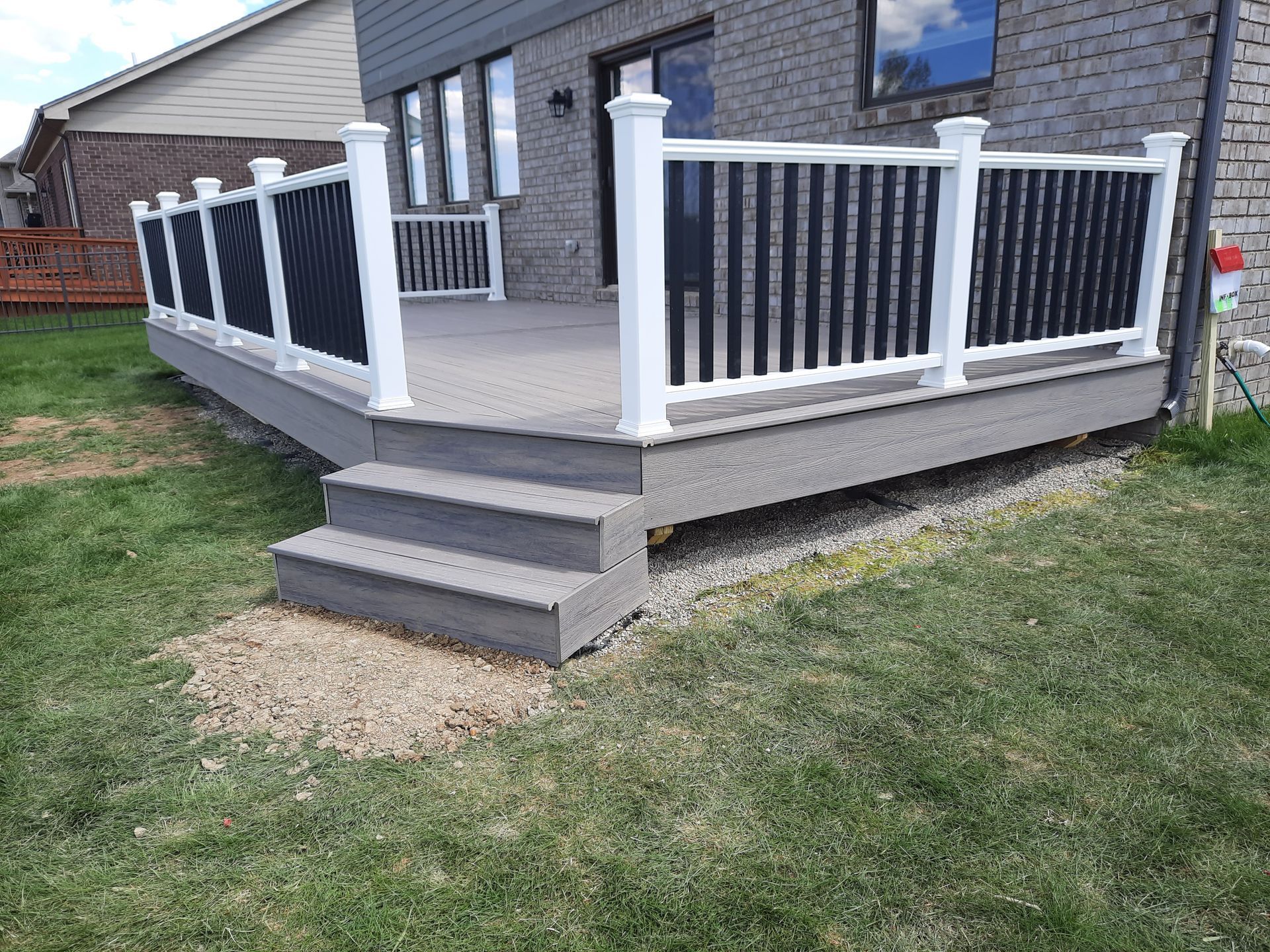 Gray deck with white railing, black vertical infill, three steps, and green lawn.