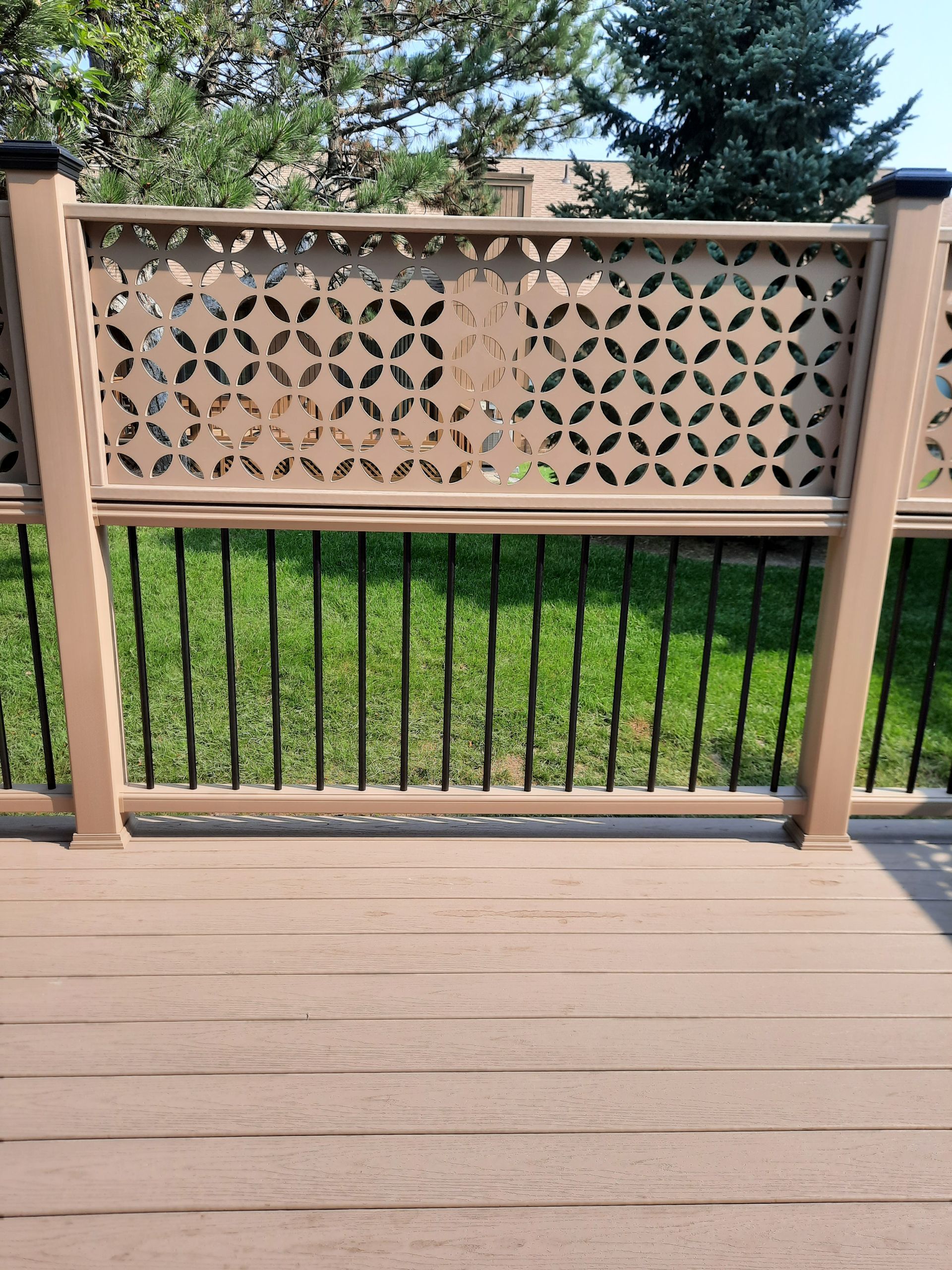 Brown deck with decorative brown lattice panel over black vertical rails, green grass background.