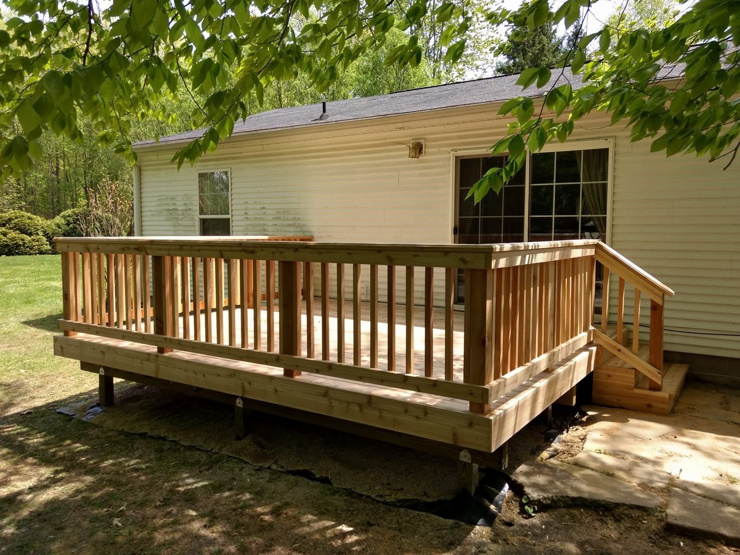 Wooden deck attached to a white house with a sliding glass door and steps, surrounded by trees.