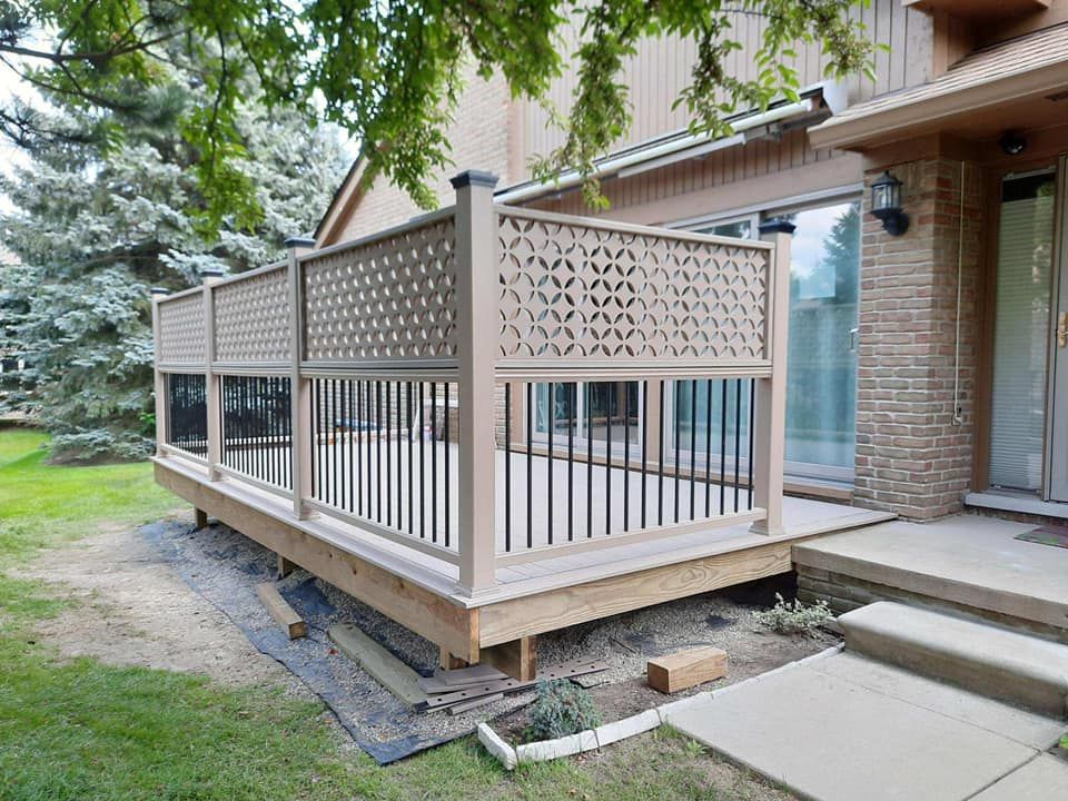 A wooden deck with beige patterned fencing, black vertical bars, and a house in the background.