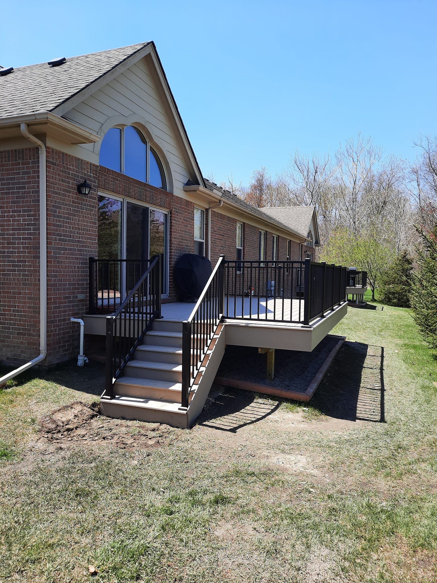 Raised deck with dark railings, stairs, and light siding on a house. Grassy yard.