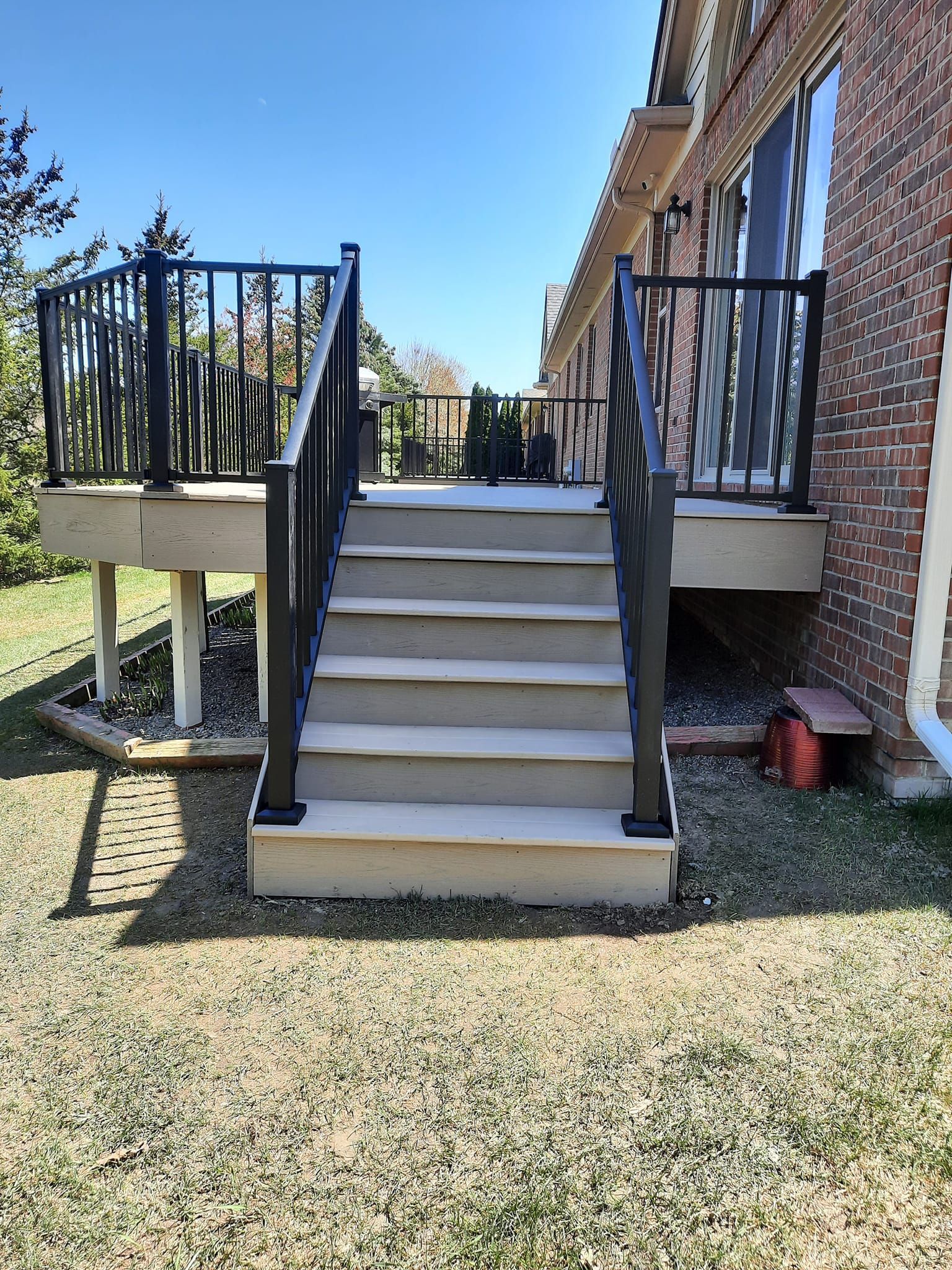 Stone steps with black railing leading up to a deck attached to a brick building, on a sunny day.