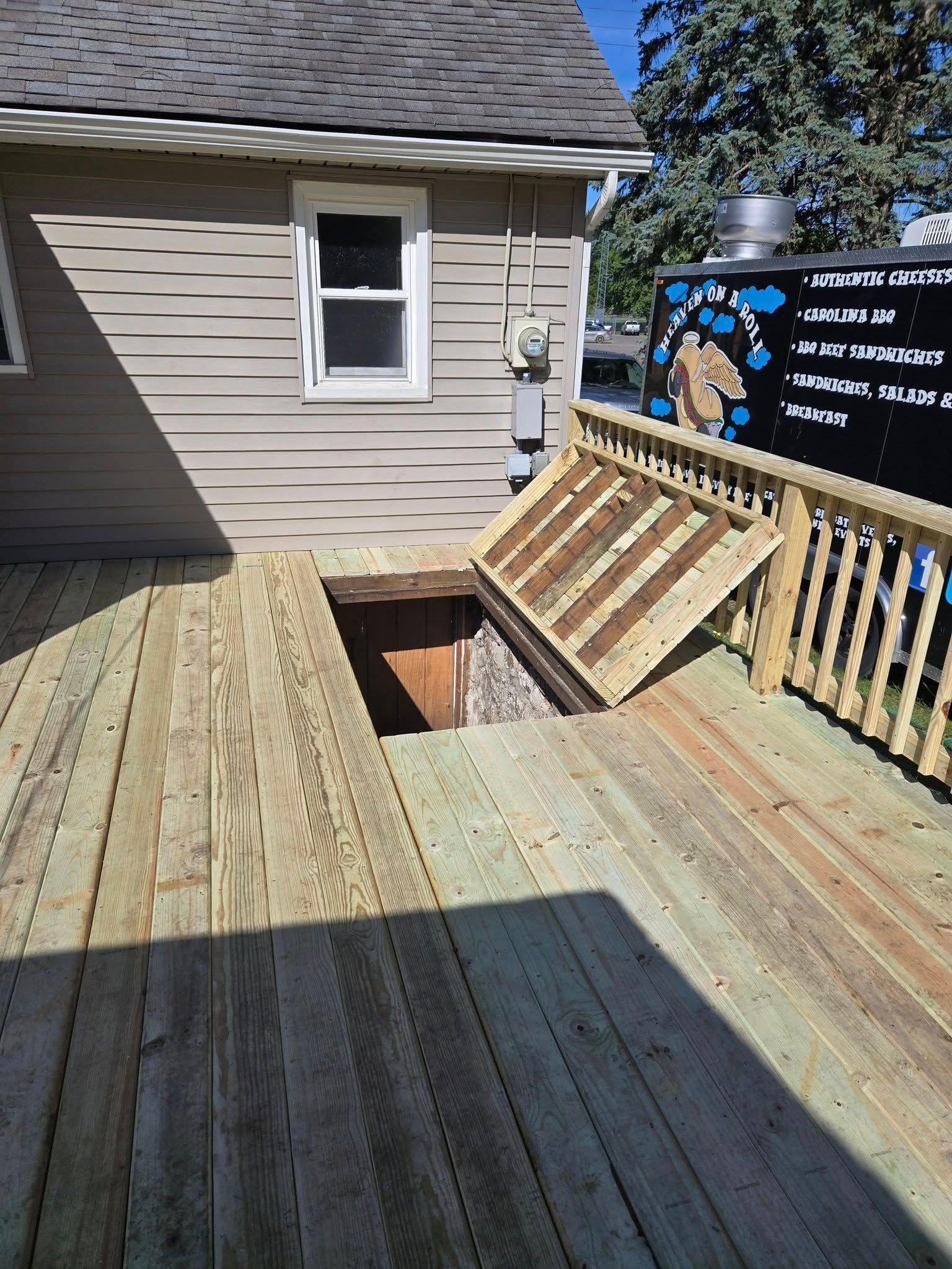 Wooden deck with a hatch leading to a basement. A building with a window is in the background.