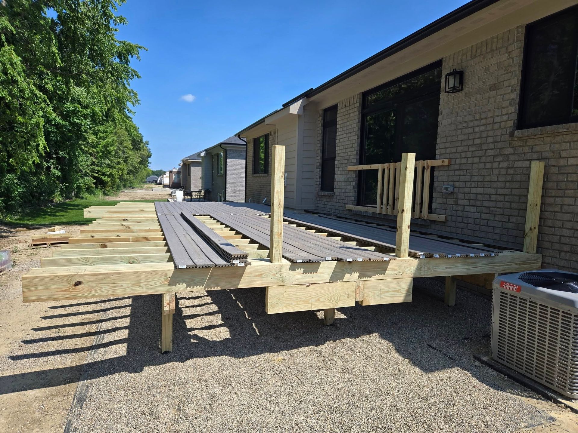 Deck under construction with gray composite boards and wooden frame, next to a brick house.