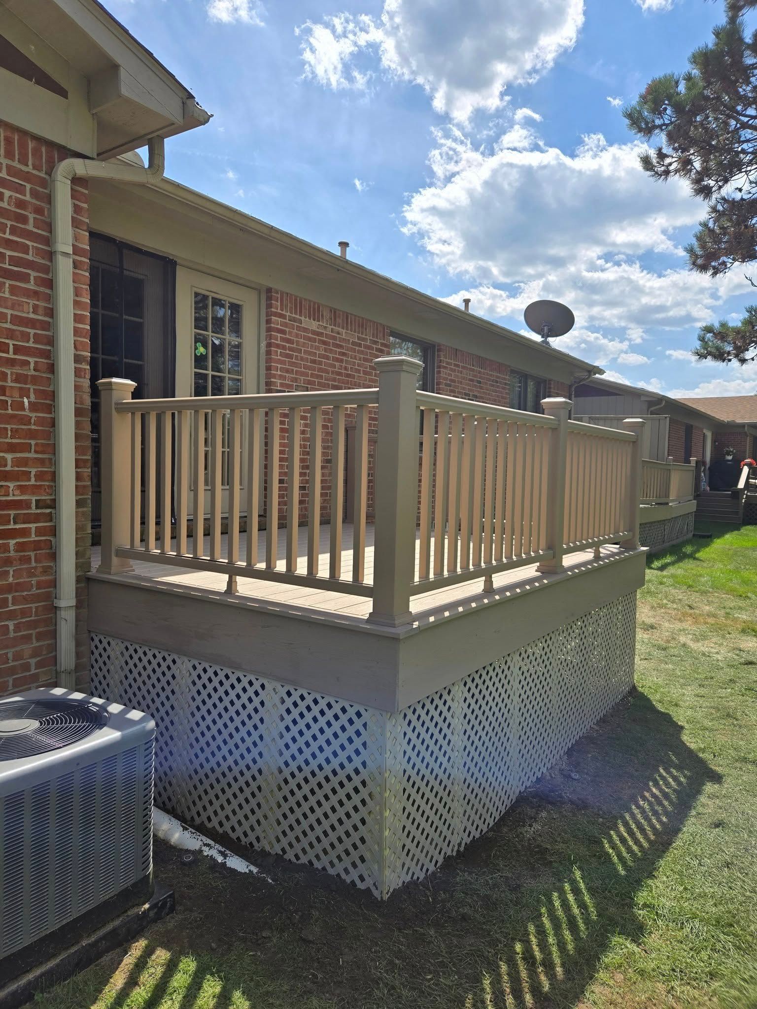 A raised wooden deck with railings attached to a brick building. Lattice underneath, blue sky.