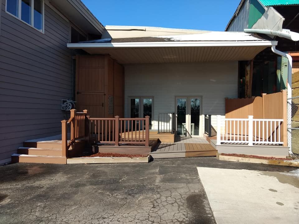 Deck with ramp and stairs leading to double doors under a covered area, next to a building.