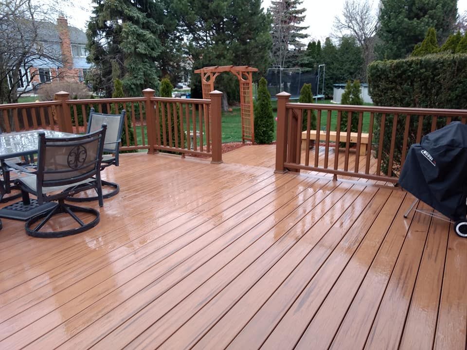 Wooden deck with railing, table with chairs, and a grill in a backyard.