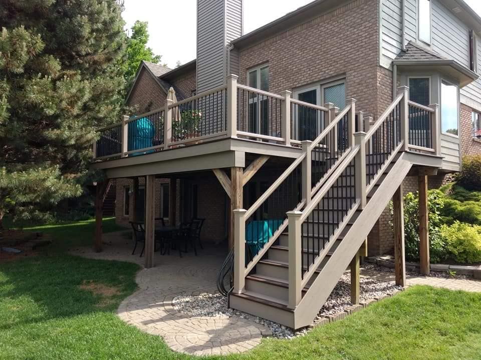 A two-story house with a wooden deck and stairs; green grass and a stone pathway.