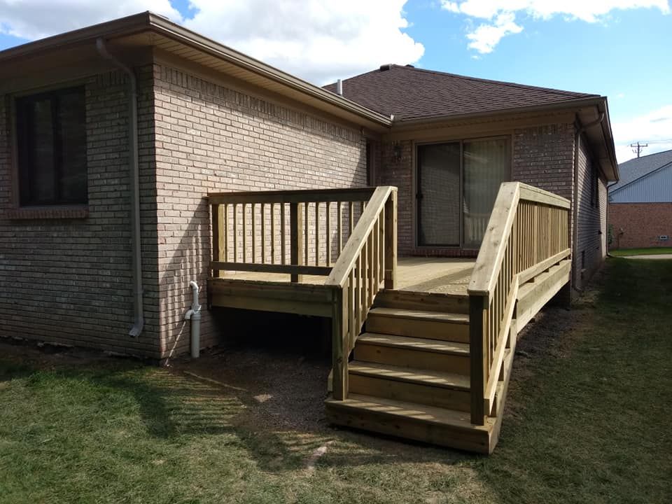 Wooden deck with stairs attached to a brick house. Green lawn surrounds the deck.
