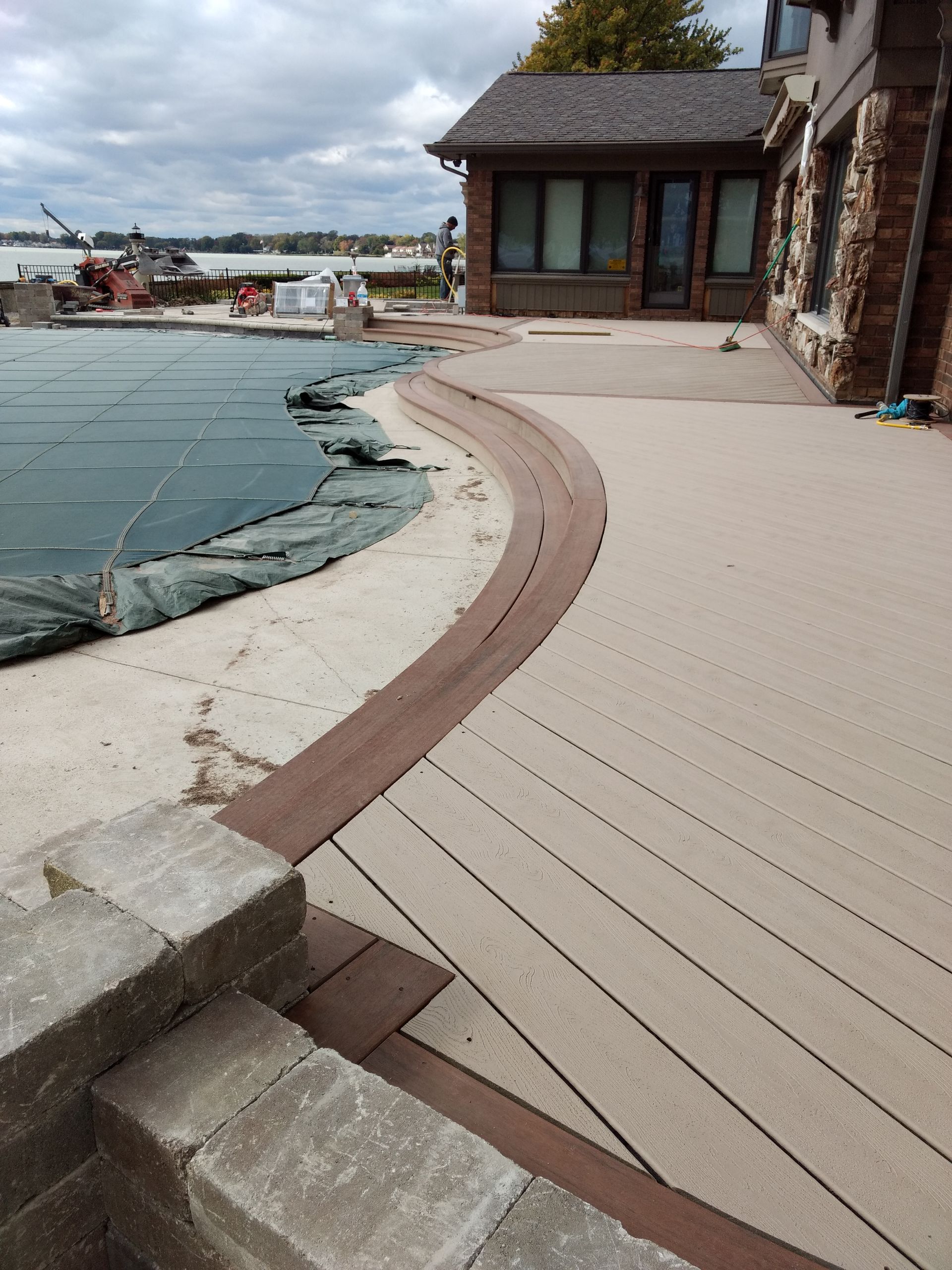 Concrete patio with brown accent borders next to a pool covered in a tarp. House in the background.