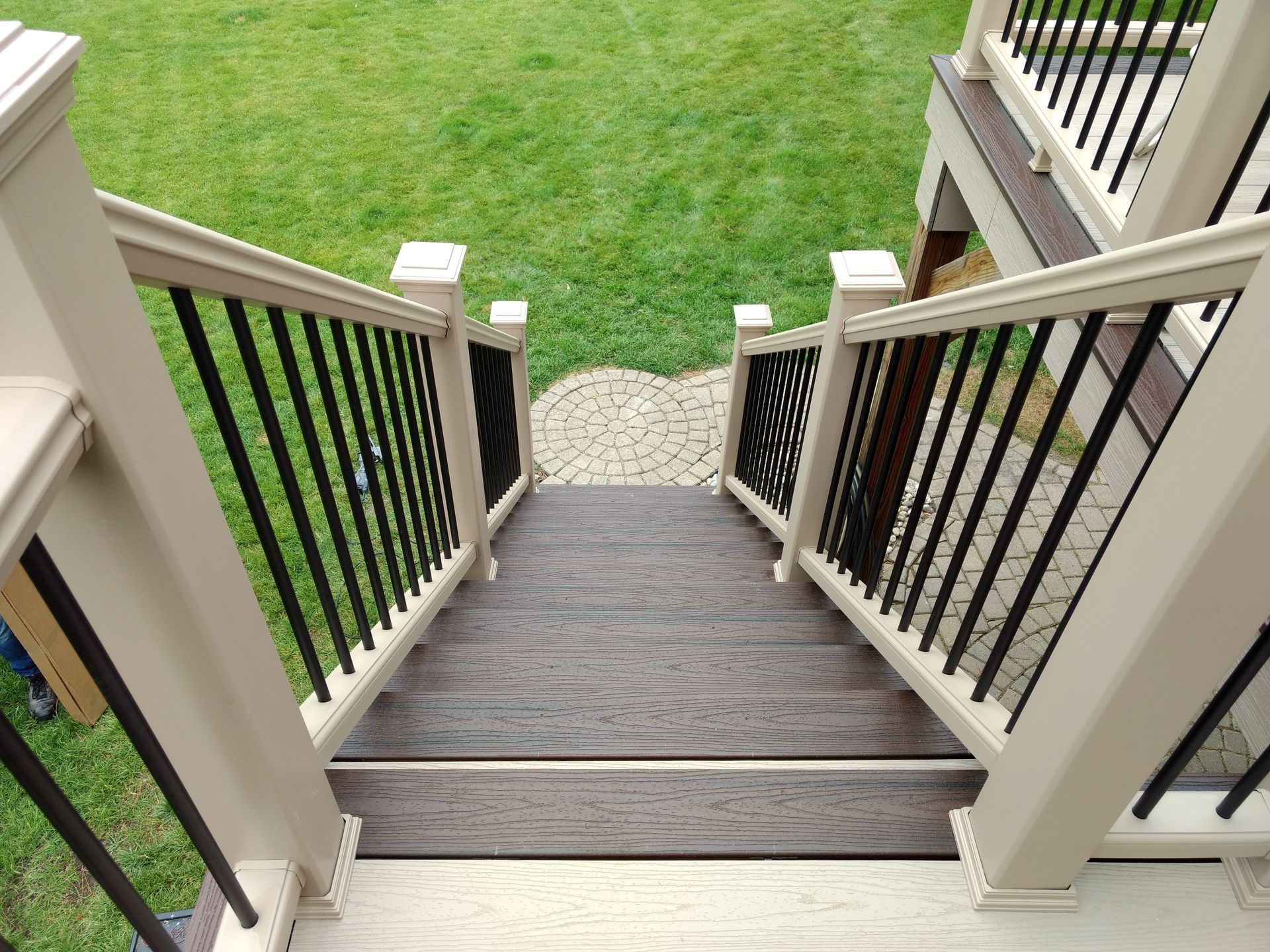 Staircase leading down to a stone patio and grassy yard. Beige railing with black balusters.