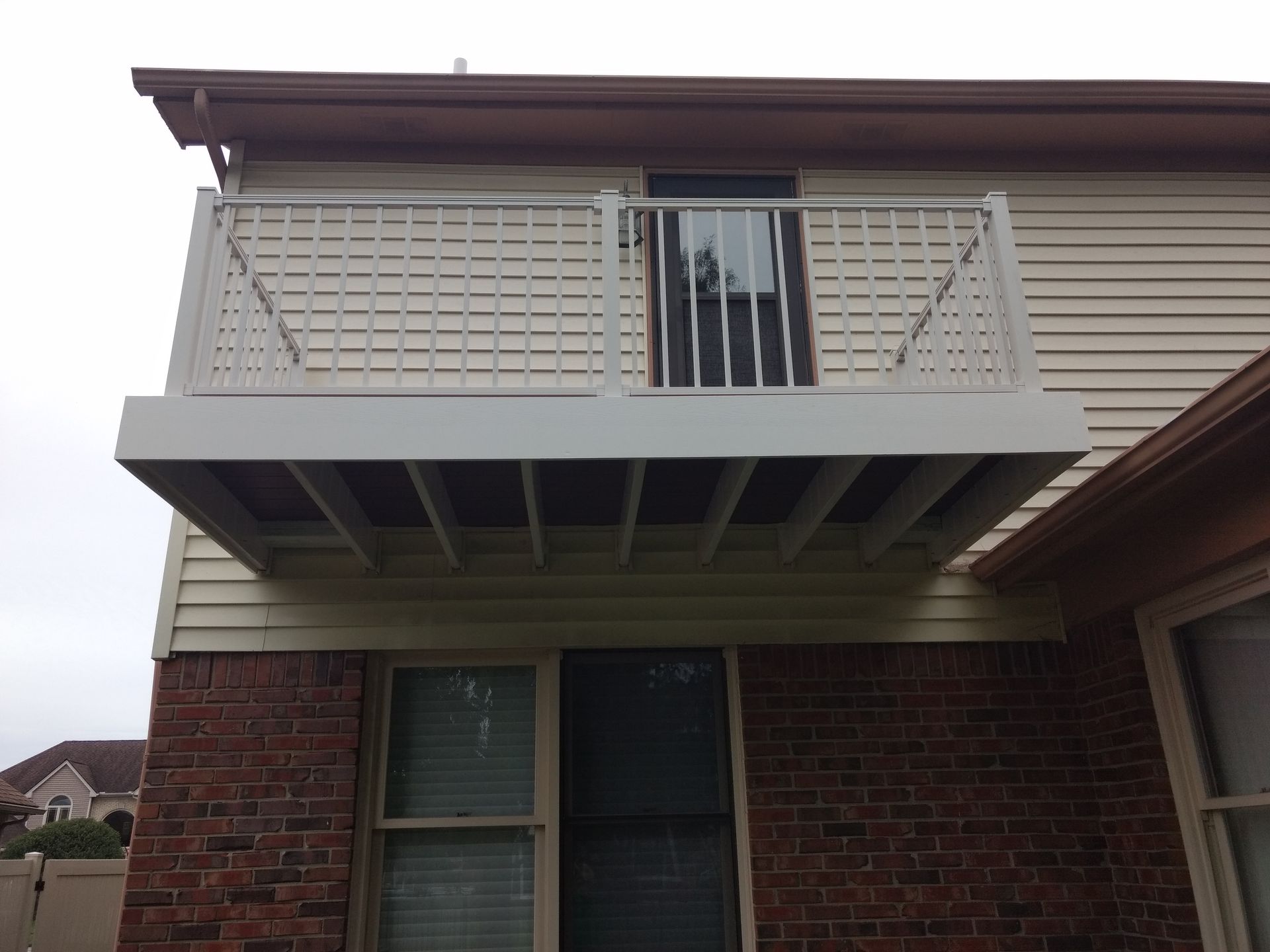 White deck with lattice railing, attached to a two-story beige house with brick facade.